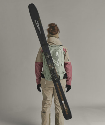 Eine Frau in Skijacke und -hose trägt Skier auf dem Rücken. Eine Frau in Skijacke und -hose trägt Skier auf dem Rücken.