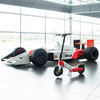 Ein McLaren-Rennwagen und ein Elektroroller stehen nebeneinander in einer Halle.