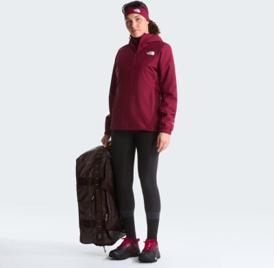 Eine Frau in einer dunkelroten Jacke hält eine braune Tasche und trägt schwarze Leggings. Eine Frau in einer dunkelroten Jacke hält eine braune Tasche und trägt schwarze Leggings.