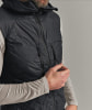 Ein Mann in einer schwarzen gesteppten Weste mit Kapuze und einem hellgrauen Langarmshirt.