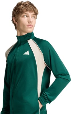 Ein Mann in einer dunkelgrünen Jacke mit beige Akzenten und Adidas-Logo auf der Brust. Ein Mann in einer dunkelgrünen Jacke mit beige Akzenten und Adidas-Logo auf der Brust.