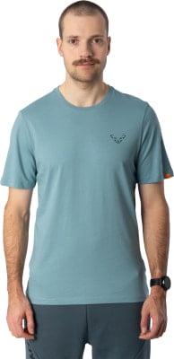 Ein Mann im blauen T-Shirt mit Logo und einer Uhr am Handgelenk posiert. Ein Mann im blauen T-Shirt mit Logo und einer Uhr am Handgelenk posiert.