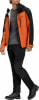 Ein Mann in einer orange-schwarzen Jacke und schwarzer Hose mit Wanderschuhen.