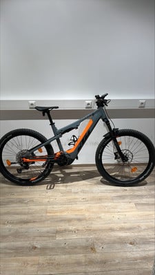Ein graues KTM E-Bike mit orangen Akzenten steht auf einem Holzboden. Ein graues KTM E-Bike mit orangen Akzenten steht auf einem Holzboden.