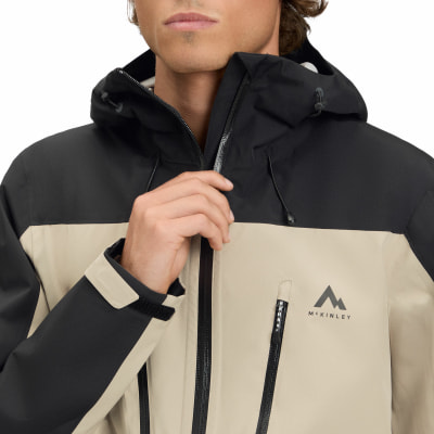 Ein Mann schließt eine beige Jacke mit schwarzen Details und Kapuze. Ein Mann schließt eine beige Jacke mit schwarzen Details und Kapuze.