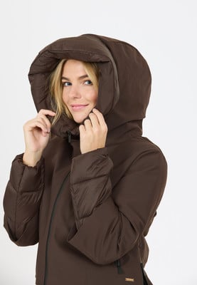 Eine Frau in einer braunen Daunenjacke mit Kapuze lächelt und hält ihre Kapuze fest. Eine Frau in einer braunen Daunenjacke mit Kapuze lächelt und hält ihre Kapuze fest.