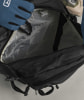 Eine Hand im blauen Handschuh greift in einen offenen schwarzen Rucksack.