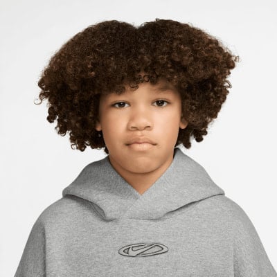 Ein Junge mit lockigem Haar trägt einen grauen Hoodie mit Nike-Logo. Ein Junge mit lockigem Haar trägt einen grauen Hoodie mit Nike-Logo.