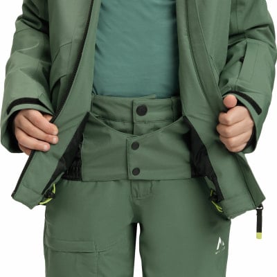 Ein Kind trägt eine grüne Winterjacke und Hose mit schwarzen Knöpfen. Ein Kind trägt eine grüne Winterjacke und Hose mit schwarzen Knöpfen.