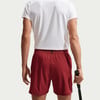 Ein Mann in einem weißen T-Shirt und weinroten Shorts hält einen Schläger.