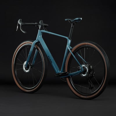 Ein modernes blaugrünes Gravelbike mit braunen Reifen und schwarzem Lenker.