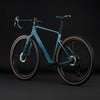 Ein modernes blaugrünes Gravelbike mit braunen Reifen und schwarzem Lenker.