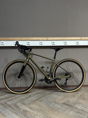 Ein grünes Gravelbike steht auf einem Holzboden vor einer grauen Wand. Ein grünes Gravelbike steht auf einem Holzboden vor einer grauen Wand.