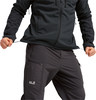 Ein Mann in einer schwarzen Jacke und dunklen Hosen zieht den Kordelzug der Jacke am Bund.