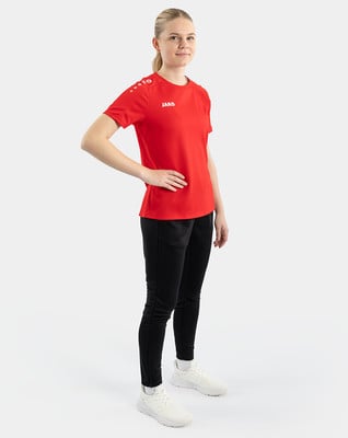 Eine Frau in einem roten T-Shirt und schwarzer Hose steht mit einer Hand in der Hüfte. Eine Frau in einem roten T-Shirt und schwarzer Hose steht mit einer Hand in der Hüfte.