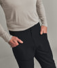 Ein Mann hat die Hände in den Taschen seiner schwarzen Hose und trägt ein hellgraues Hemd.