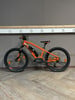 Ein orangefarbenes E-Bike mit schwarzen Rädern steht auf einem Holzboden.