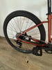 Das Hinterrad eines orangefarbenen Fahrrads mit Kette und Pedal auf Holzboden.