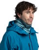 Ein Mann in einer blauen Jacke mit einem bedruckten Schlauchtuch und lockigen Haaren.