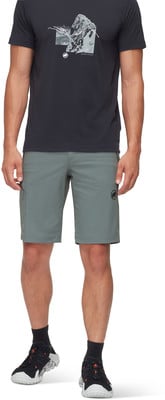 Ein Mann in einem schwarzen T-Shirt mit Aufdruck und grauer Hose mit Mammut-Logo.