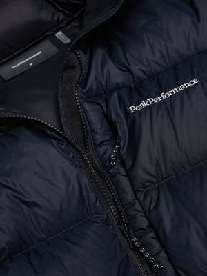Detail einer dunklen Daunenjacke mit Peak Performance Logo und Reißverschluss.