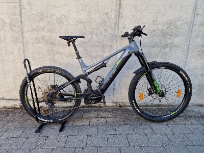 Ein graues Genesis E-Mountainbike mit schwarzen und grünen Akzenten, das auf einem Gehweg steht. Ein graues Genesis E-Mountainbike mit schwarzen und grünen Akzenten, das auf einem Gehweg steht.