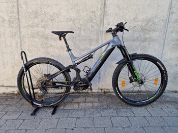 Ein graues Genesis E-Mountainbike mit schwarzen und grünen Akzenten, das auf einem Gehweg steht.