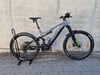 Ein graues Genesis E-Mountainbike mit schwarzen und grünen Akzenten, das auf einem Gehweg steht.