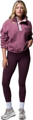 Eine Frau in einem rosafarbenen Fleece-Pullover und dunklen Leggings mit Turnschuhen.