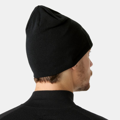 Fekete kötött sapka, a tetején anyag ráncolva, egy férfi fején.