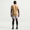 Ein Mann in einem beigen T-Shirt und grauen Shorts steht mit dem Rücken zur Kamera.