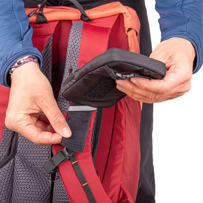 Eine Hand schließt eine kleine schwarze Tasche am Rucksackgurt mit Klettverschluss.