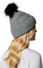 Mädchen mit blonden Haaren und einer grauen Mütze mit schwarzem Bommel.