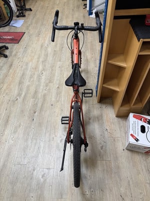 Ein orangefarbenes Fahrrad steht auf einem Holzboden neben einem Regal.