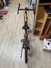 Ein orangefarbenes Fahrrad steht auf einem Holzboden neben einem Regal.