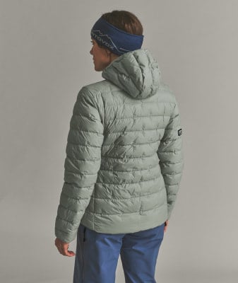 Frau in einer Daunenjacke und blauer Mütze mit Logo, Rücken zum Betrachter. Frau in einer Daunenjacke und blauer Mütze mit Logo, Rücken zum Betrachter.