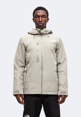 Muž v béžové bundě The North Face s kapucí a bílým logem na hrudi. Muž v béžové bundě The North Face s kapucí a bílým logem na hrudi.