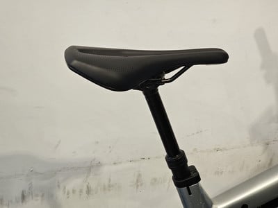 Schwarze Fahrradsattelstütze mit schwarzem Sattel und weißer Wand im Hintergrund.