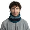 Ein Mann mit lockigem Haar trägt einen grauen Pullover und einen bunten Schal.