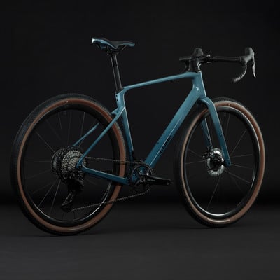 Modernes blaugrünes Gravelbike mit braunen Reifen vor schwarzem Hintergrund.