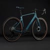 Modernes blaugrünes Gravelbike mit braunen Reifen vor schwarzem Hintergrund.