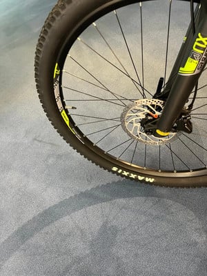 Detail eines Mountainbike-Rades mit Federgabel und Scheibenbremse auf blauem Teppich. Detail eines Mountainbike-Rades mit Federgabel und Scheibenbremse auf blauem Teppich.