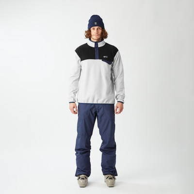 Ein Mann in Skibekleidung mit blauer Mütze und hellgrauem Fleece-Pullover.