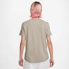 Rückansicht einer Frau mit pinken Haaren in einem beigen T-Shirt und weißer Hose.