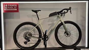 Ein hellgraues Cube Gravelbike mit schwarzem Lenker und Sattel auf einem Ständer.