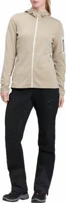 Frau in beigefarbener Kapuzenjacke und schwarzer Hose mit vielen Taschen.