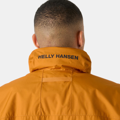 Egy férfi narancssárga kabátban, Helly Hansen logóval a galléron, hátulról. Egy férfi narancssárga kabátban, Helly Hansen logóval a galléron, hátulról.