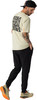 Ein Mann in einem beigefarbenen T-Shirt mit Aufdruck und schwarzer Hose, trägt Laufschuhe.
