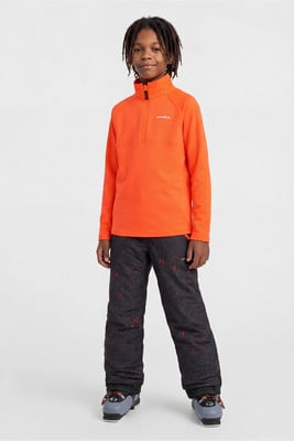 Junge im orangefarbenen Fleece-Pullover und dunkler Skihose mit Skischuhen. Junge im orangefarbenen Fleece-Pullover und dunkler Skihose mit Skischuhen.