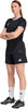 Eine Frau in schwarzem Fußballtrikot und Shorts mit weißen Socken und Fußballschuhen.